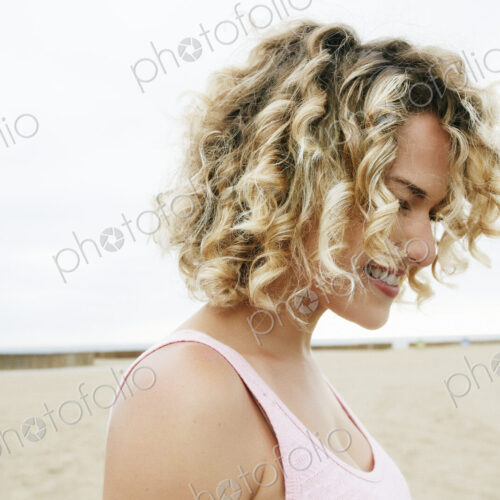 Portrait of smiling young woman with blond curly hair standing on sandy beach. Portrait of smiling young woman with blond curly hair standing on sandy beach.