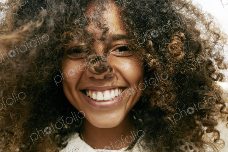 Portrait of smiling young woman with brown curly hair, looking at camera.
