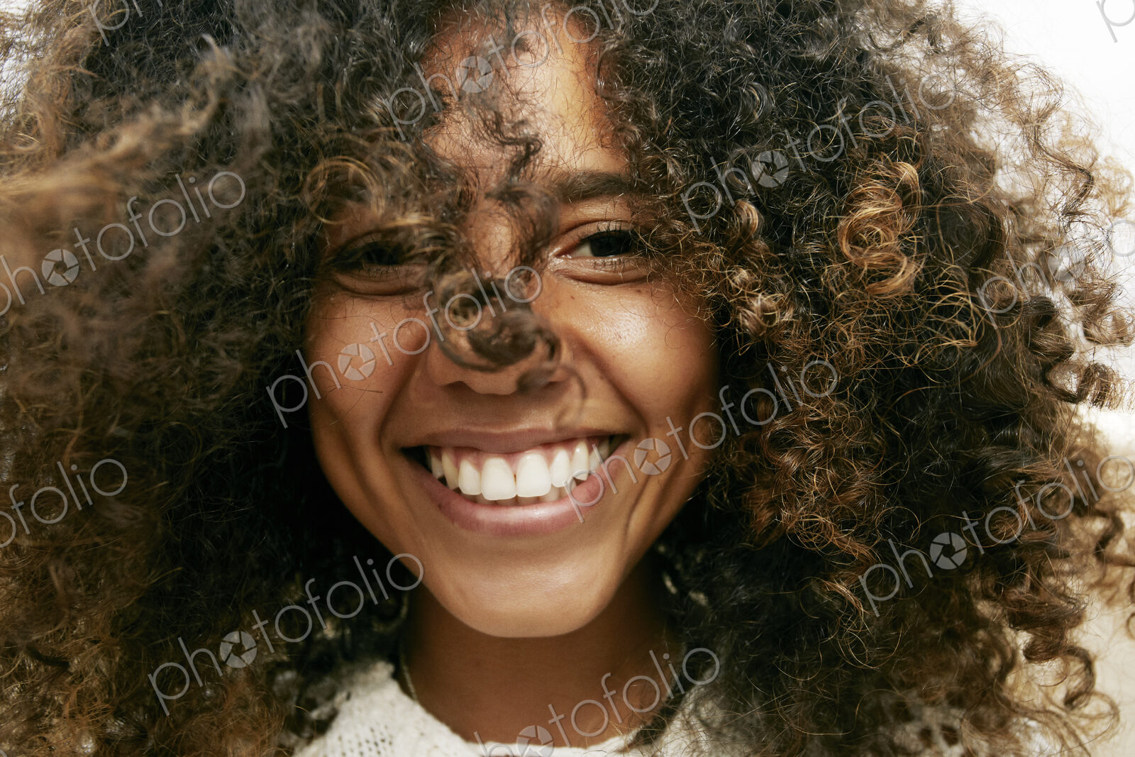 Portrait of smiling young woman with brown curly hair, looking at camera.