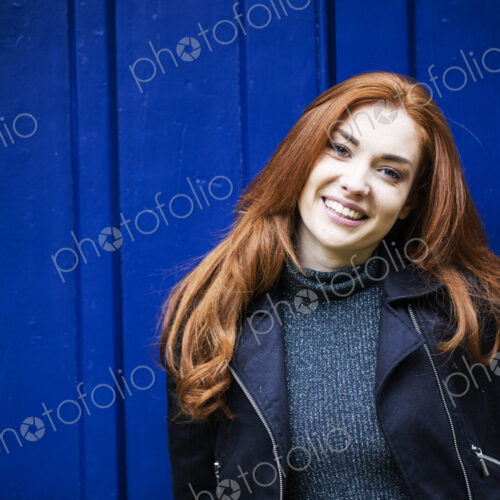Portrait of smiling young woman with long red hair in front of bright blue door.