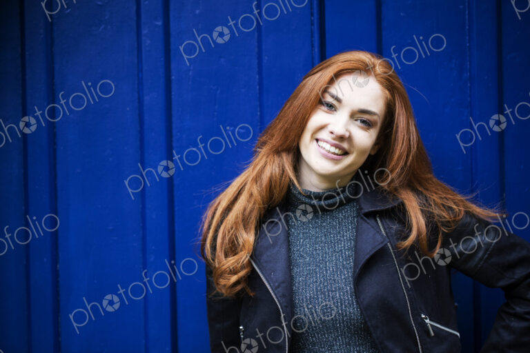 Portrait of smiling young woman with long red hair in front of bright blue door.