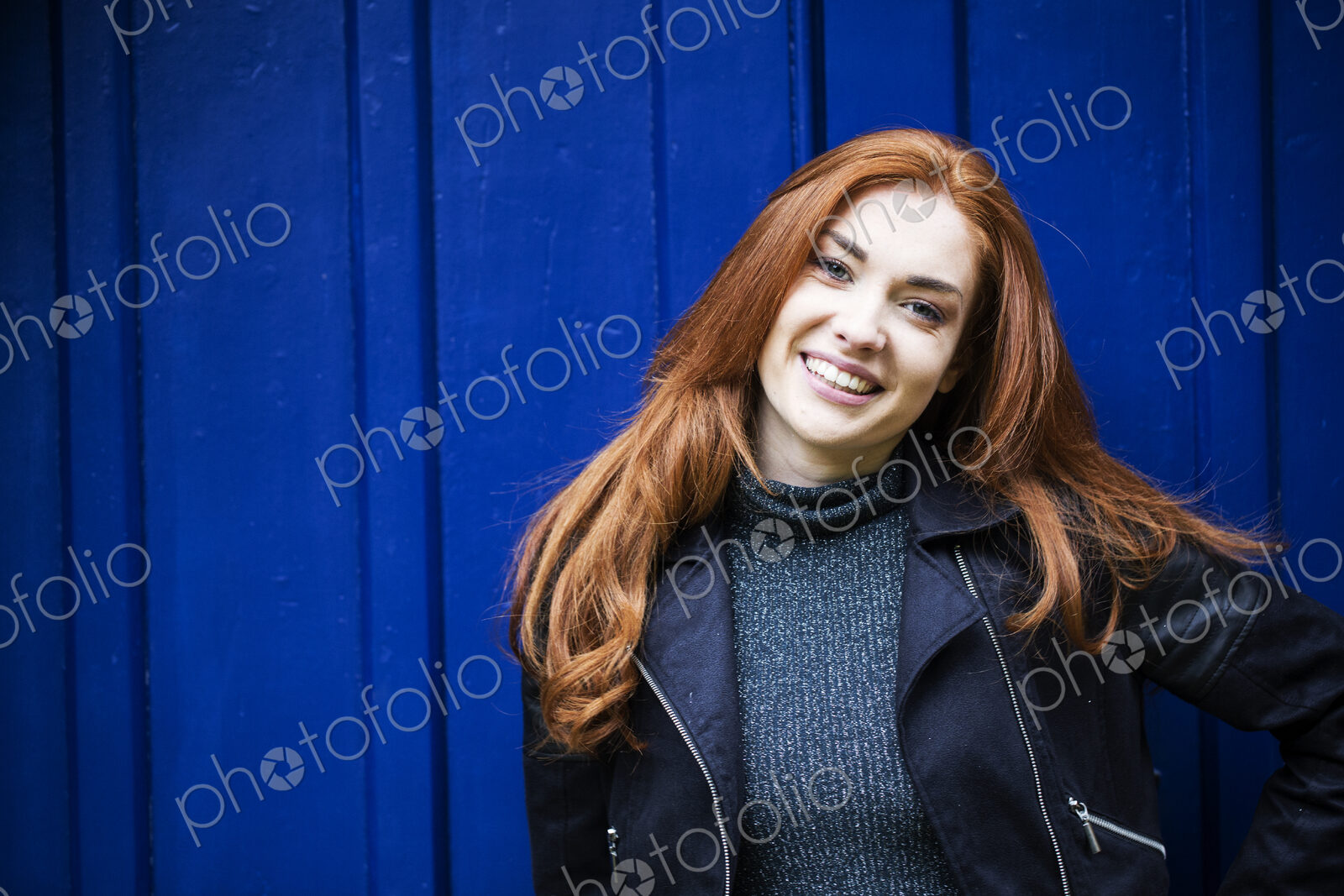 Portrait of smiling young woman with long red hair in front of bright blue door.