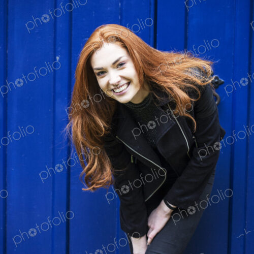 Portrait of smiling young woman with long red hair in front of bright blue door.