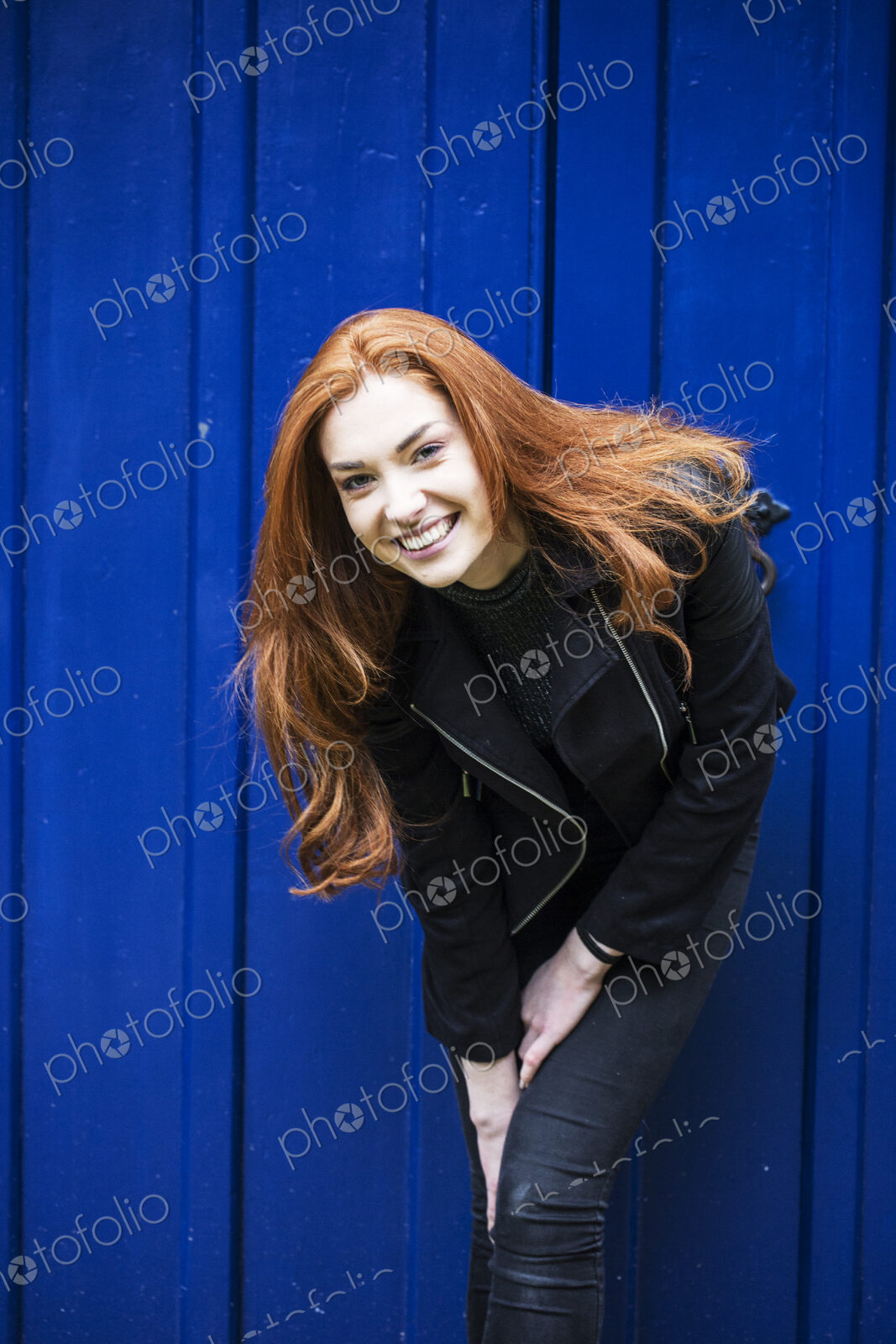 Portrait of smiling young woman with long red hair in front of bright blue door.