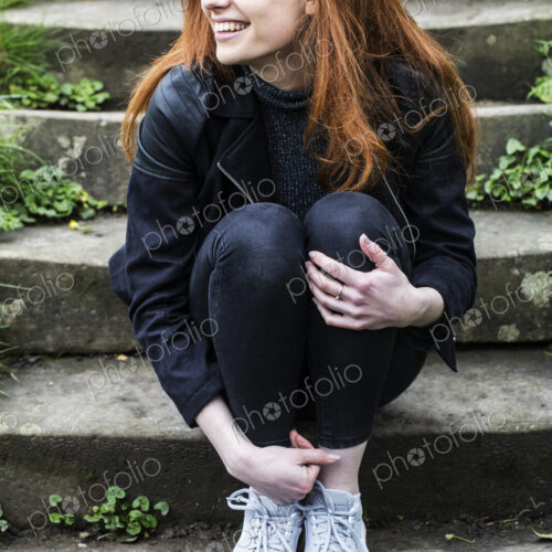 Portrait of smiling young woman with long red hair, sitting on steps outdoors.