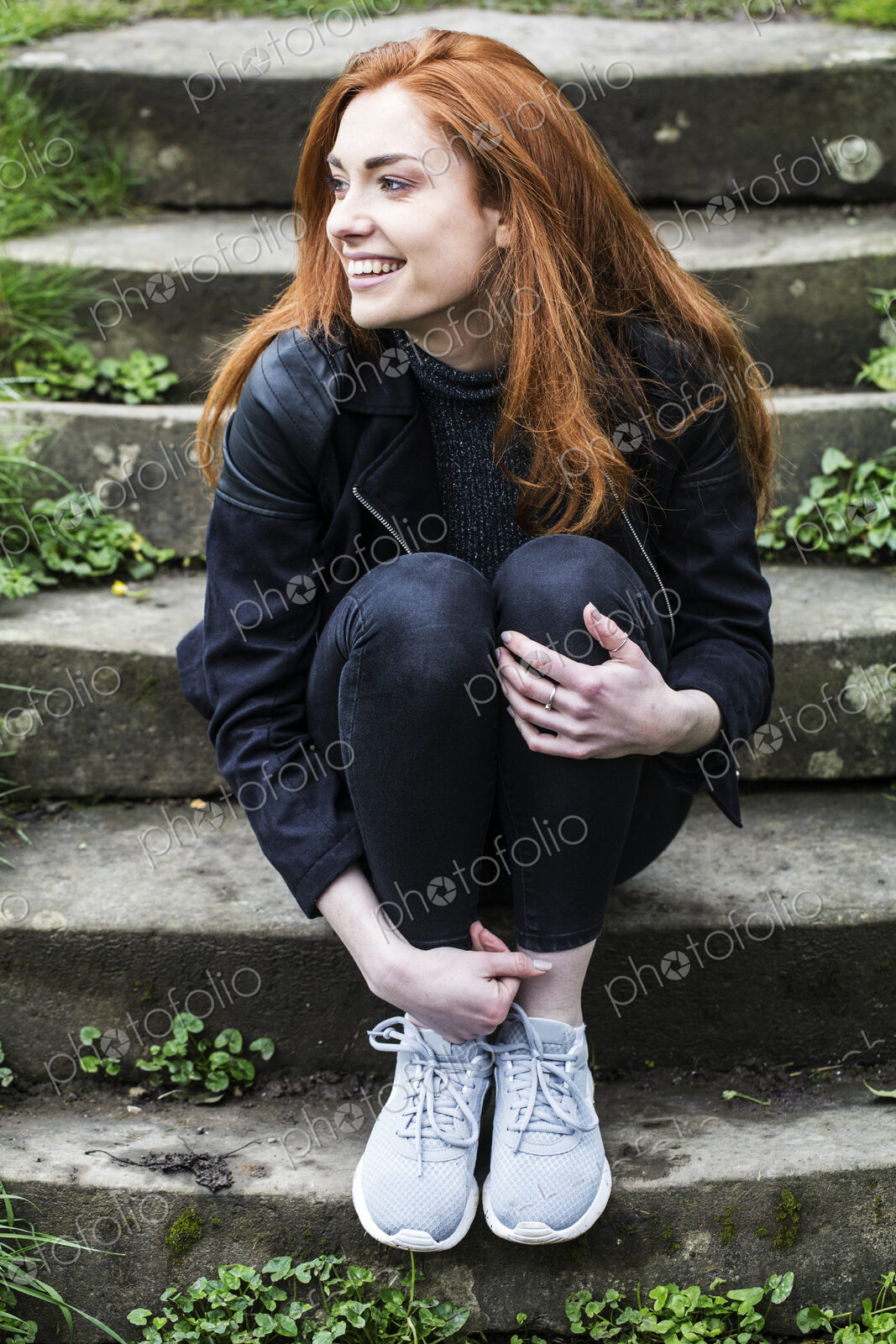 Portrait of smiling young woman with long red hair, sitting on steps outdoors.