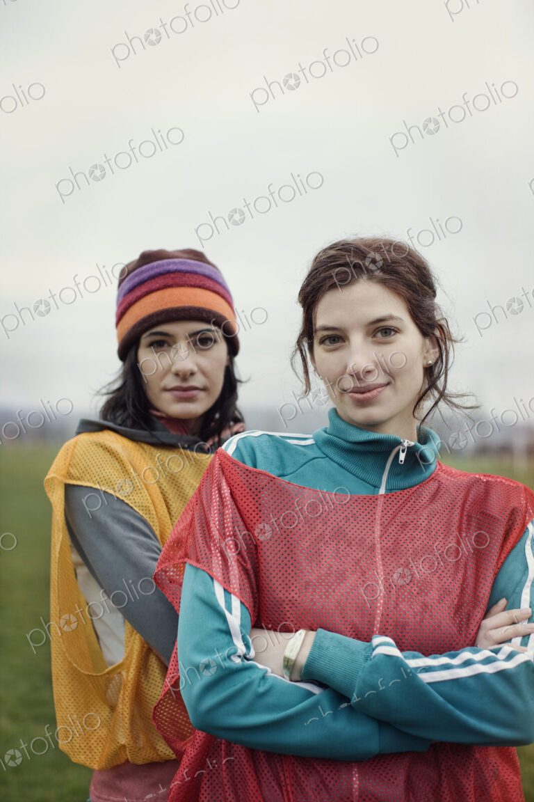 Portrait of two Caucasian women in sports clothing with team bibs of opposing teams…