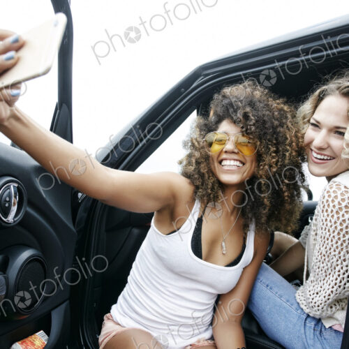 Portrait of two smiling young women sitting in car, taking selfie with mobile phone. Portrait of two smiling young women sitting in car, taking selfie with mobile phone.