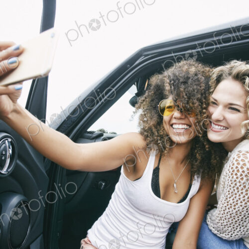 Portrait of two smiling young women sitting in car, taking selfie with mobile phone. Portrait of two smiling young women sitting in car, taking selfie with mobile phone.