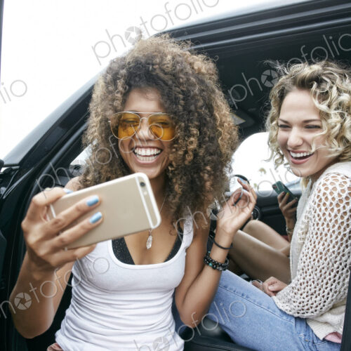 Portrait of two smiling young women sitting in car, taking selfie with mobile phone. Portrait of two smiling young women sitting in car, taking selfie with mobile phone.