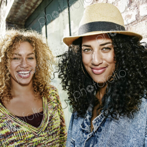 Portrait of two smiling young women with long curly black and blond hair, looking at…