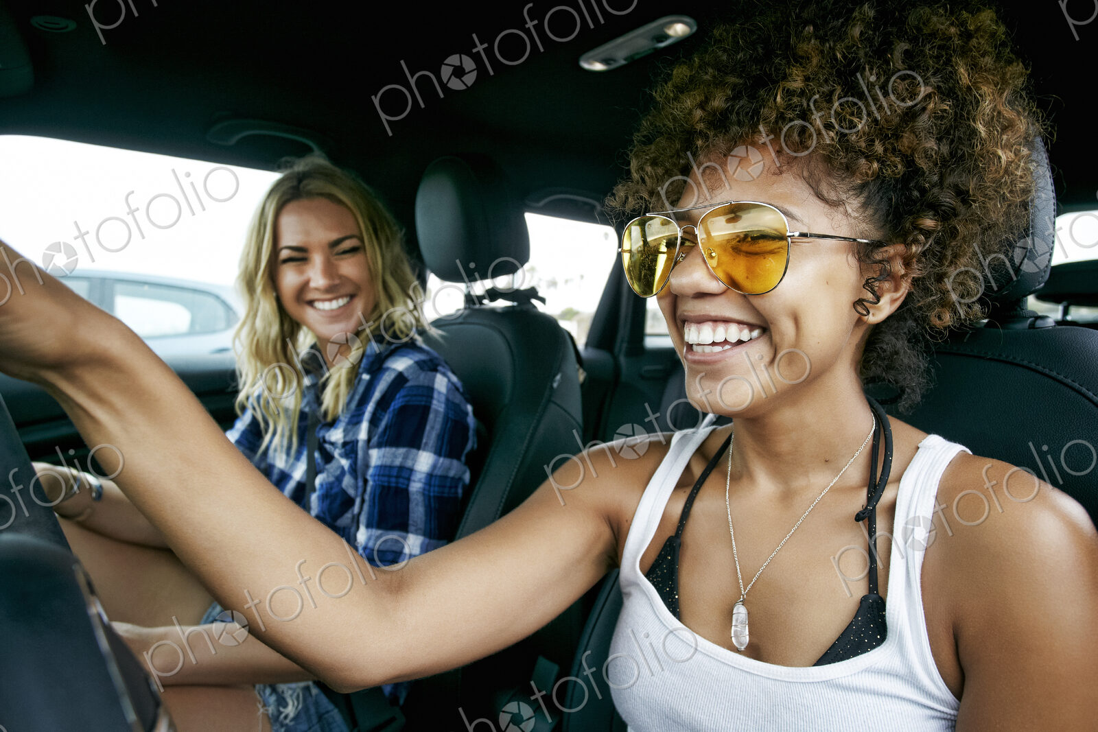Portrait of two women sitting in car, wearing sunglasses, smiling.