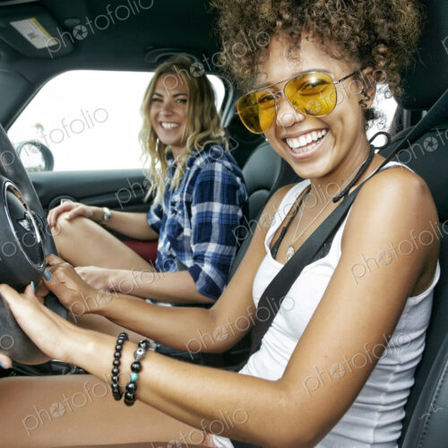 Portrait of two women with long blond and brown curly hair sitting in car, wearing… Portrait of two women with long blond and brown curly hair sitting in car, wearing…