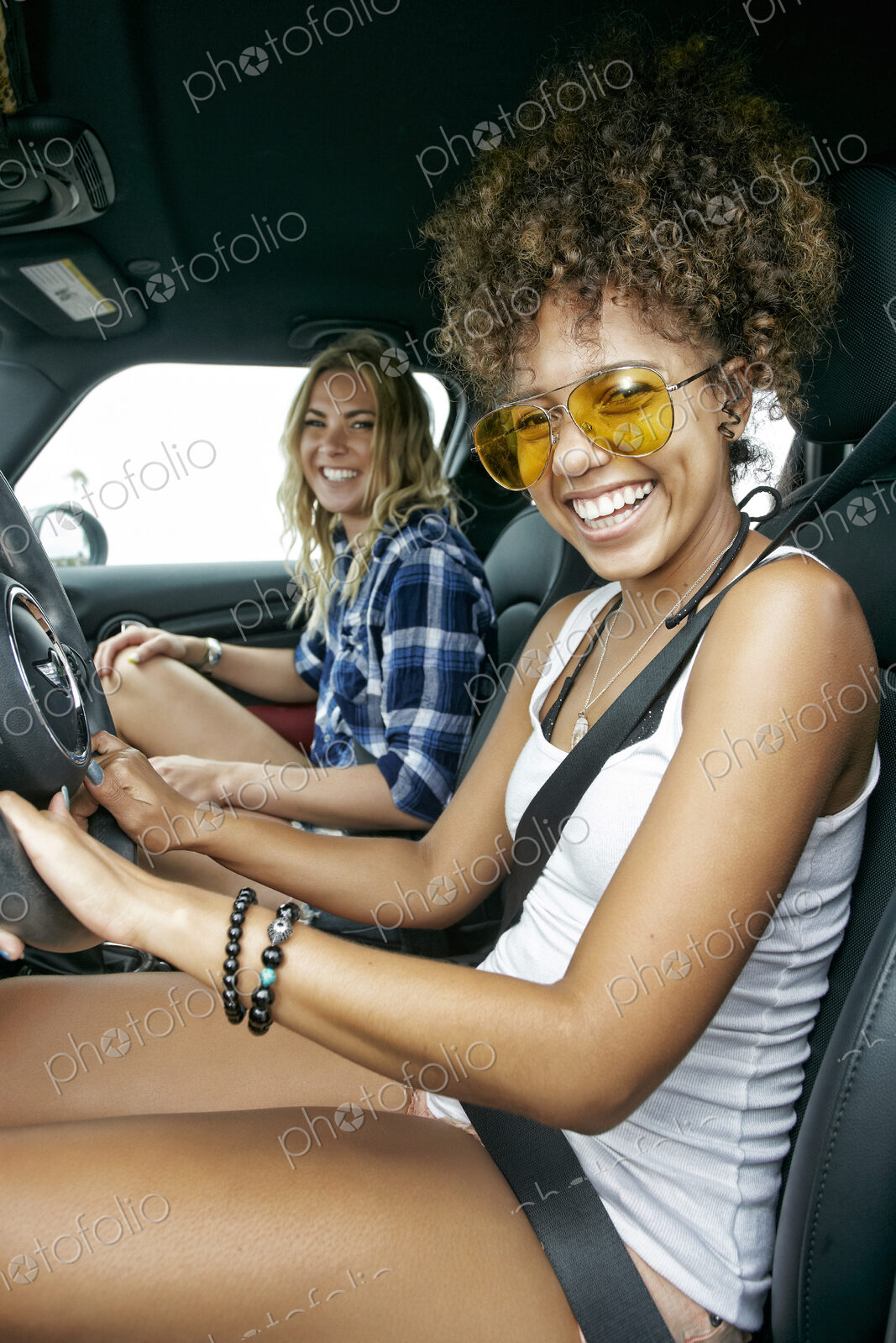 Portrait of two women with long blond and brown curly hair sitting in car, wearing…