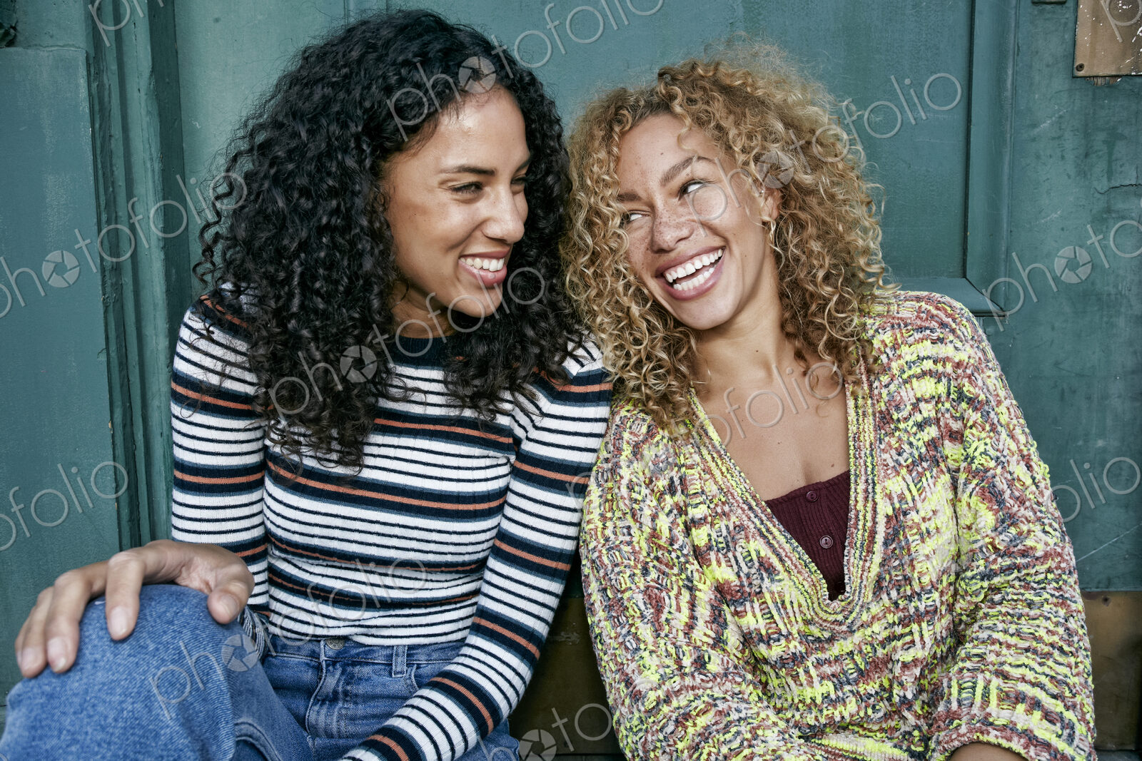Portrait of two young smiling women with long curly black and blond hair, smiling and…