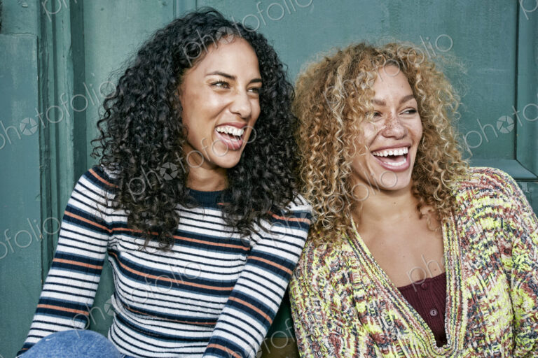 Portrait of two young smiling women with long curly black and blond hair, smiling and…