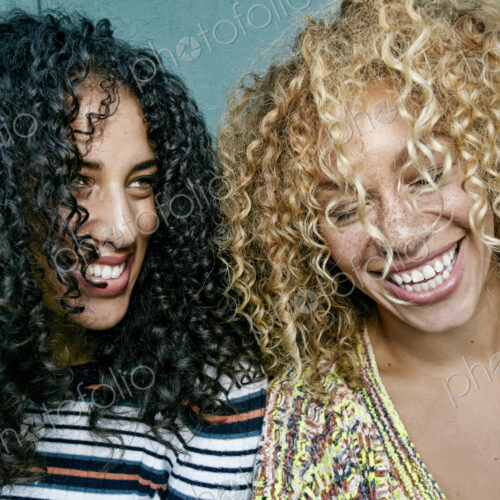 Portrait of two young women with long curly black and blond hair, smiling and laughing. Portrait of two young women with long curly black and blond hair, smiling and laughing.