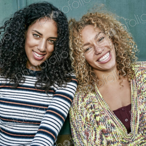 Portrait of two young women with long curly black and blond hair, smiling at camera. Portrait of two young women with long curly black and blond hair, smiling at camera.