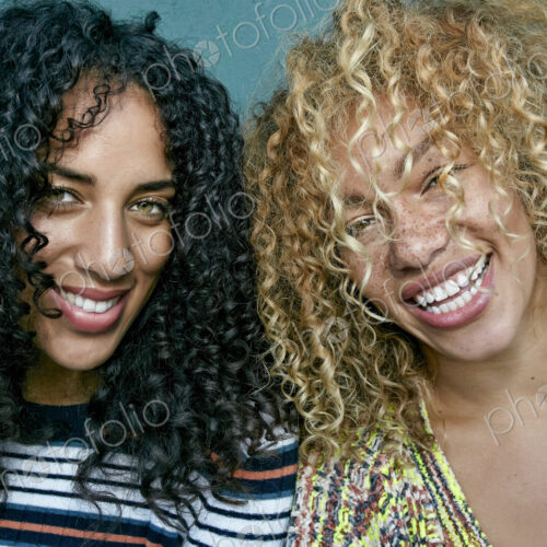 Portrait of two young women with long curly black and blond hair, smiling at camera. Portrait of two young women with long curly black and blond hair, smiling at camera.