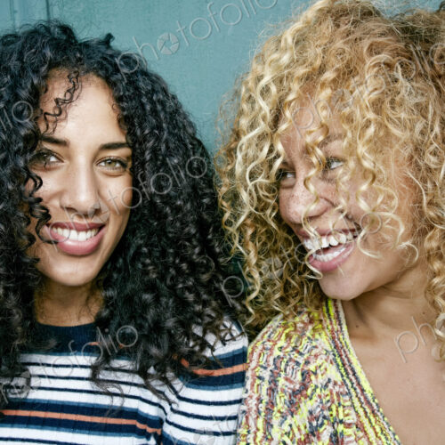 Portrait of two young women with long curly black and blond hair, smiling at camera. Portrait of two young women with long curly black and blond hair, smiling at camera.