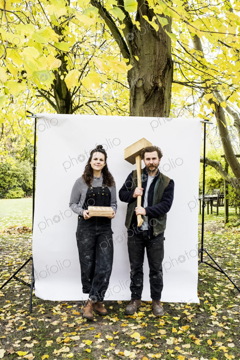 Portrait of woman and bearded man holding wooden blocks standing in front of white…