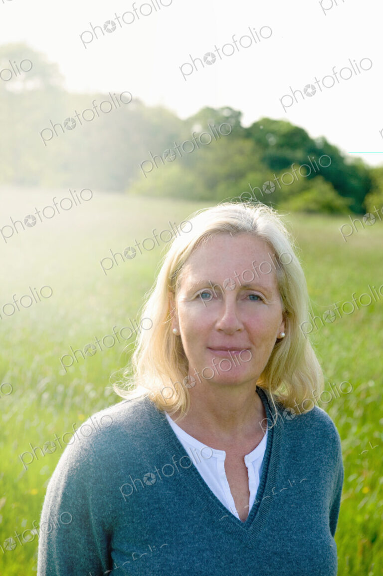 Portrait of woman with blond hair standing outdoors on a meadow, looking at camera.