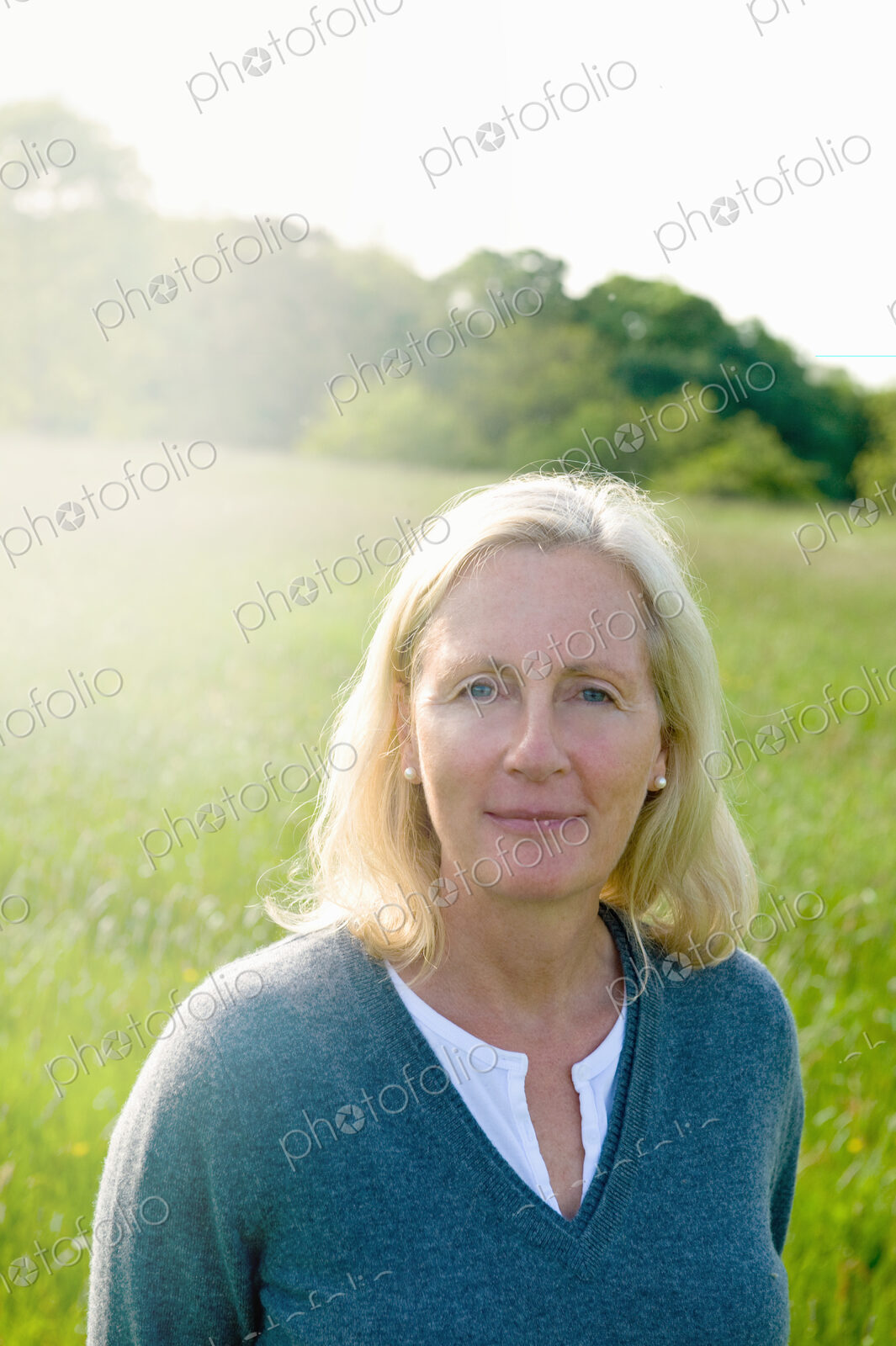 Portrait of woman with blond hair standing outdoors on a meadow, looking at camera.