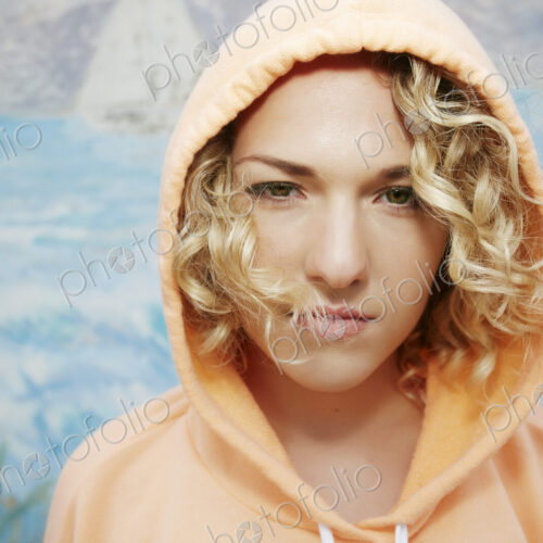 Portrait of woman with curly blond hair wearing pink hoodie, looking at camera. Portrait of woman with curly blond hair wearing pink hoodie, looking at camera.