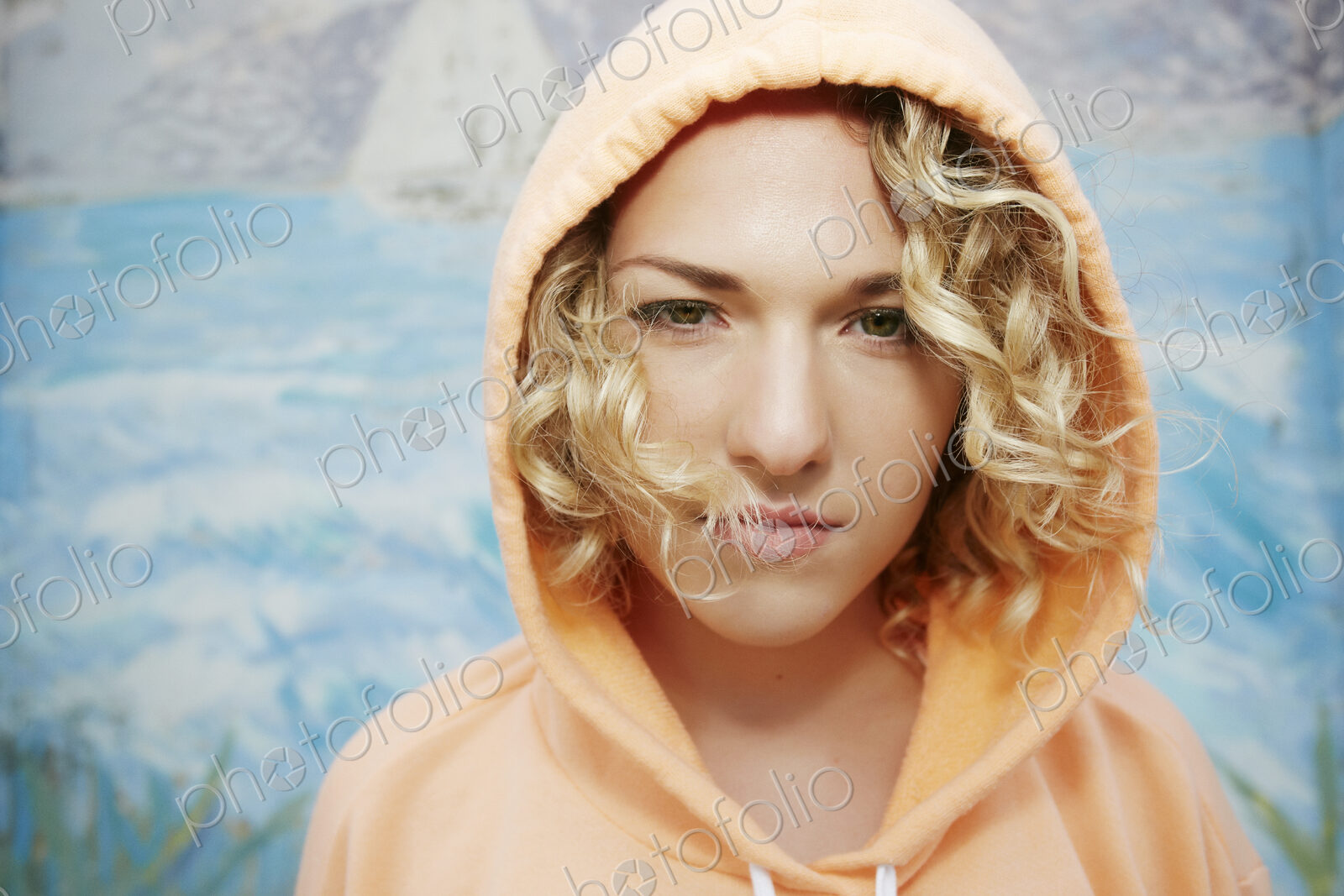 Portrait of woman with curly blond hair wearing pink hoodie, looking at camera.