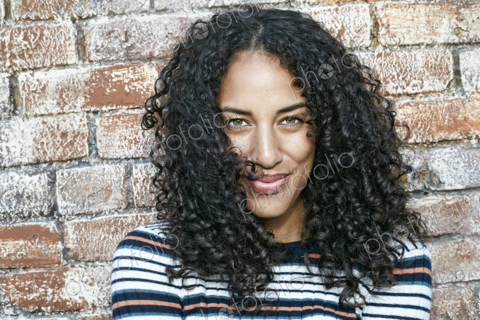 Portrait of young smiling woman with long curly black hair, looking at camera.
