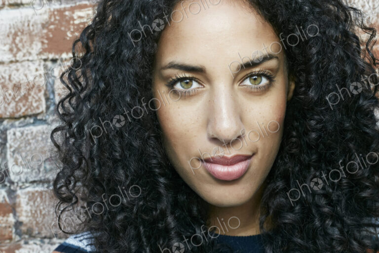 Portrait of young smiling woman with long curly black hair looking at camera.