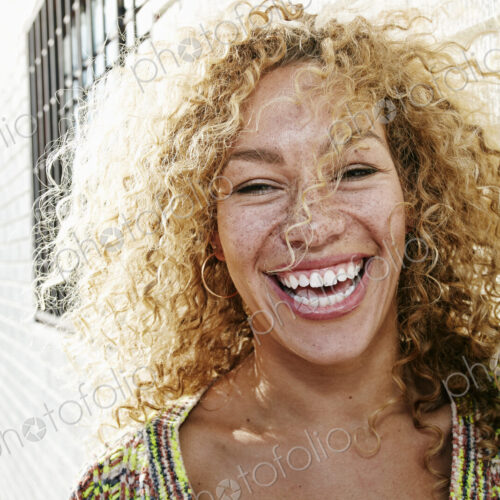 Portrait of young smiling woman with long curly blond hair, looking at camera.