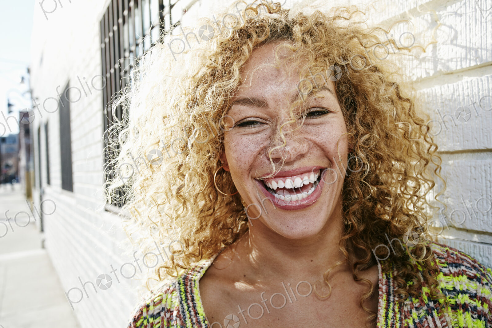 Portrait of young smiling woman with long curly blond hair, looking at camera.