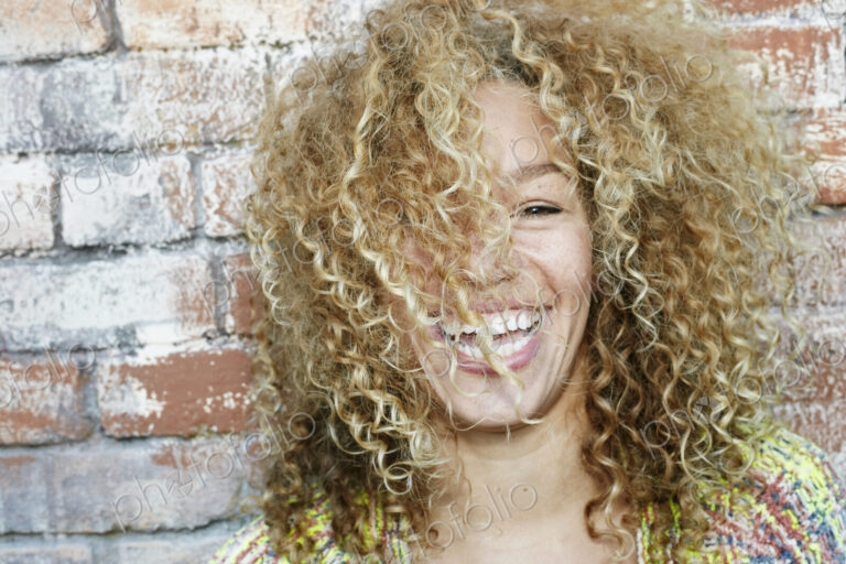 Portrait of young smiling woman with long curly blond hair, looking at camera.
