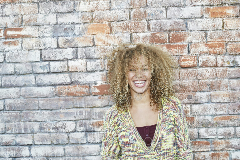 Portrait of young smiling woman with long curly blond hair, looking at camera.