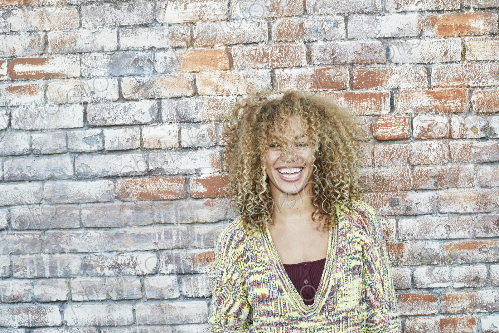Portrait of young smiling woman with long curly blond hair, looking at camera.