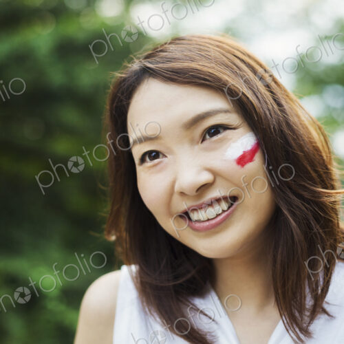 Portrait of young woman with brown hair, Japanese flag painted on her cheek, smiling…