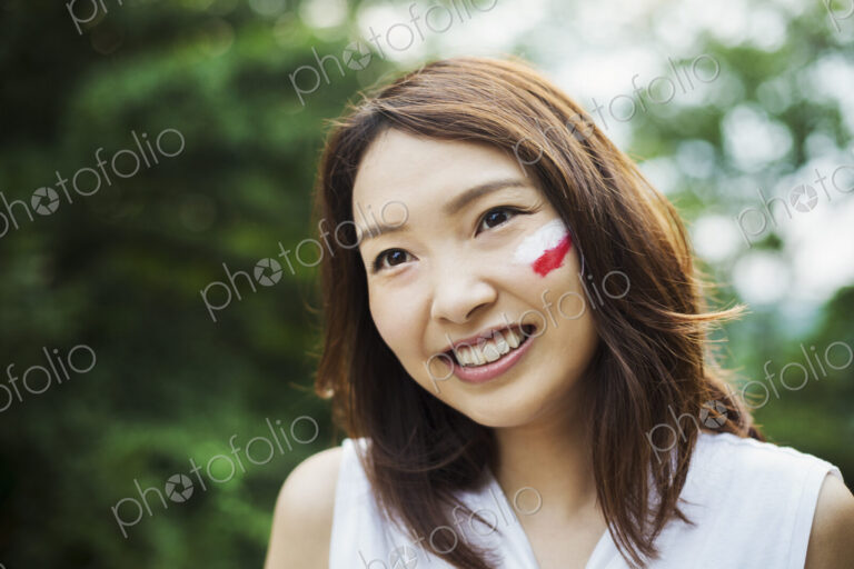 Portrait of young woman with brown hair, Japanese flag painted on her cheek, smiling…