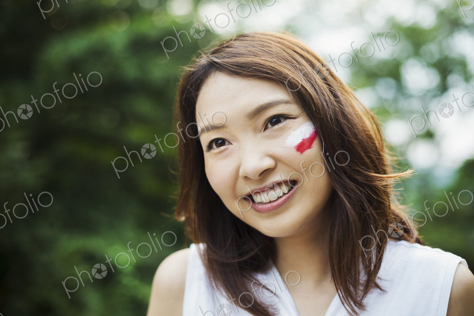 Portrait of young woman with brown hair, Japanese flag painted on her cheek, smiling…
