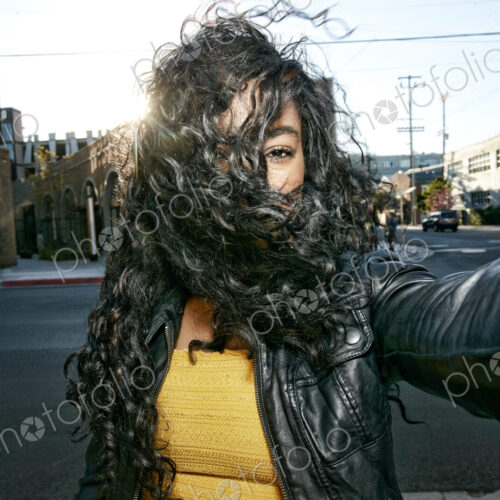 Portrait of young woman with long curly black hair standing on street, looking at camera. Portrait of young woman with long curly black hair standing on street, looking at camera.