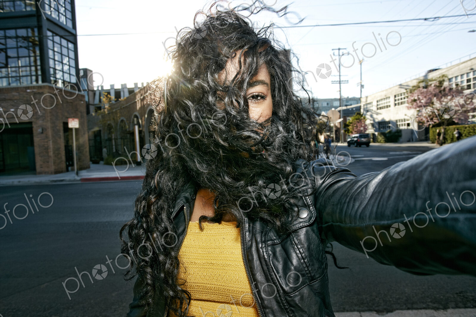 Portrait of young woman with long curly black hair standing on street, looking at camera.