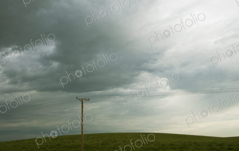 Power lines running through prairie and grassland with cloudy sky above.