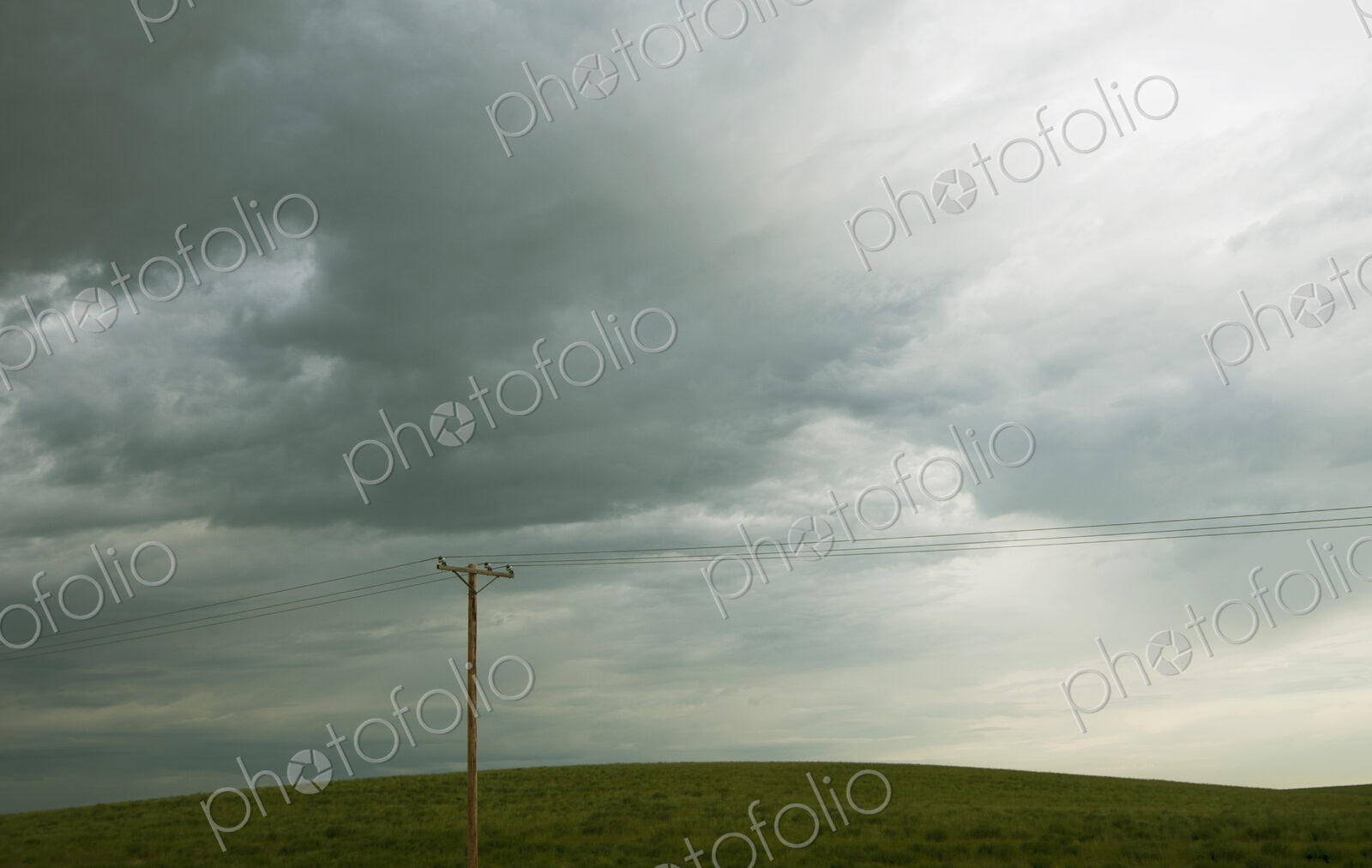 Power lines running through prairie and grassland with cloudy sky above.