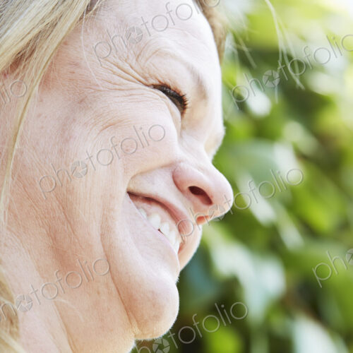 Profile of a blond mature woman standing outdoors.