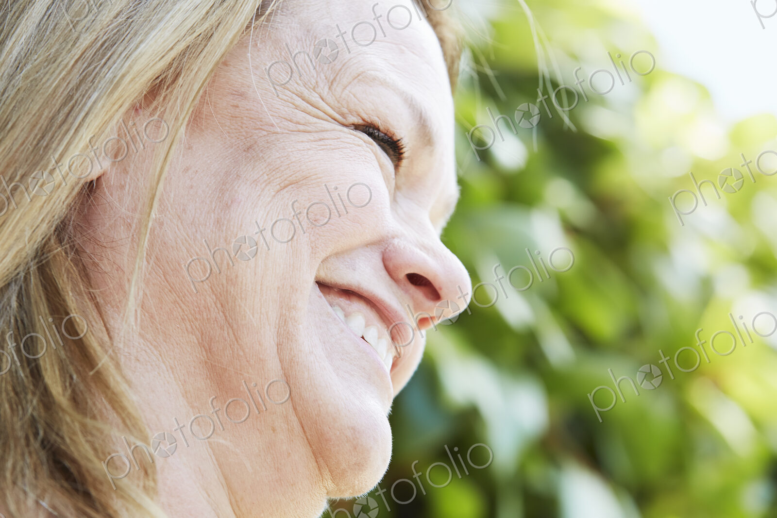 Profile of a blond mature woman standing outdoors.
