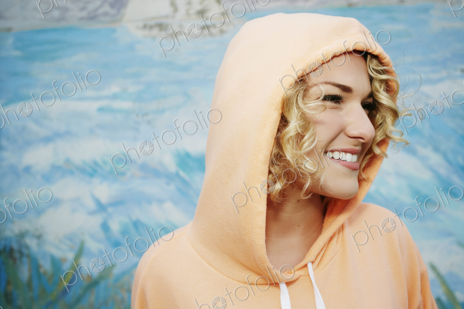 Profile portrait of smiling woman with curly blond hair wearing pink hoodie.