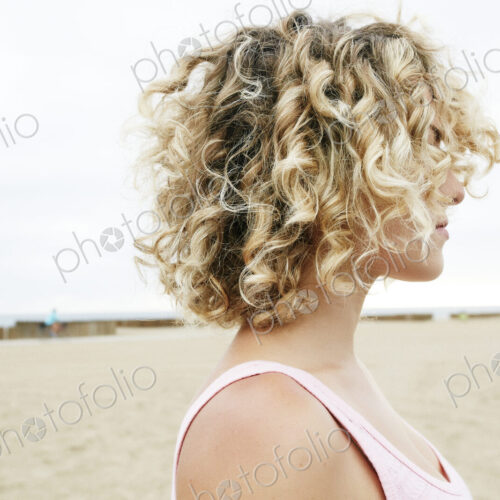 Profile portrait of young woman with blond curly hair standing on sandy beach. Profile portrait of young woman with blond curly hair standing on sandy beach.