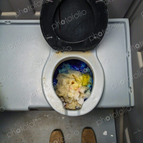 Public reststop toilet, view from above of a dirty blocked bowl full of toilet paper.