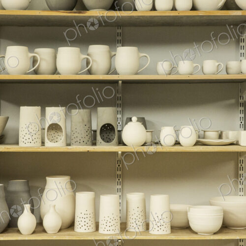 Racks of hand thrown hand crafted pottery vases and objects on shelves in the drying room. Racks of hand thrown hand crafted pottery vases and objects on shelves in the drying room.