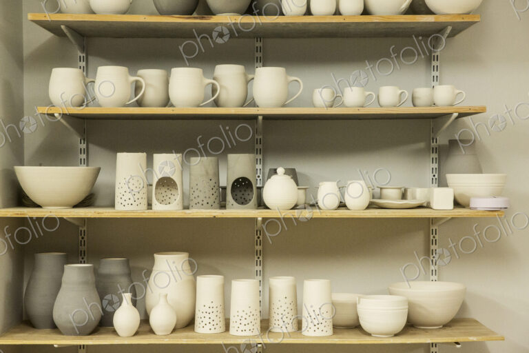 Racks of hand thrown hand crafted pottery vases and objects on shelves in the drying room.